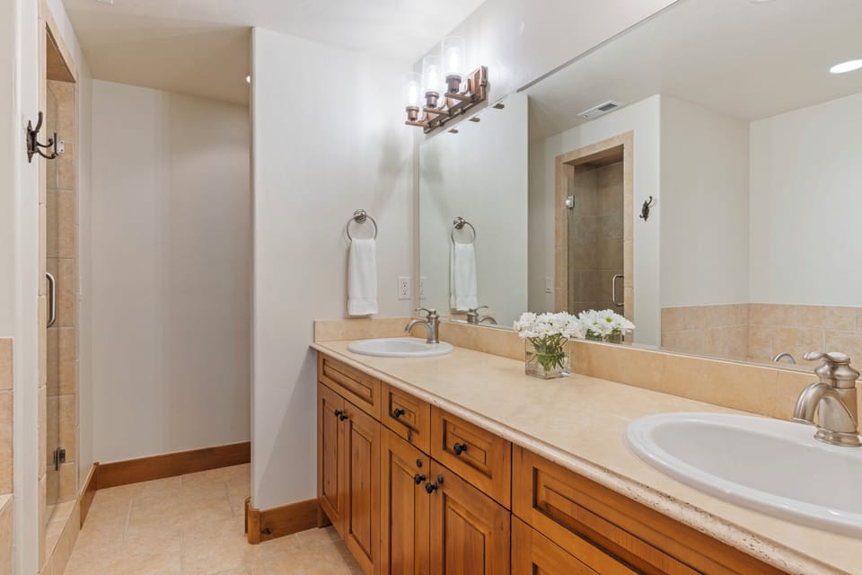 Your spacious bathroom features dual sinks with elegant stone countertops and warm wood cabinetry, creating the perfect space for you and your travel companion to get ready together.