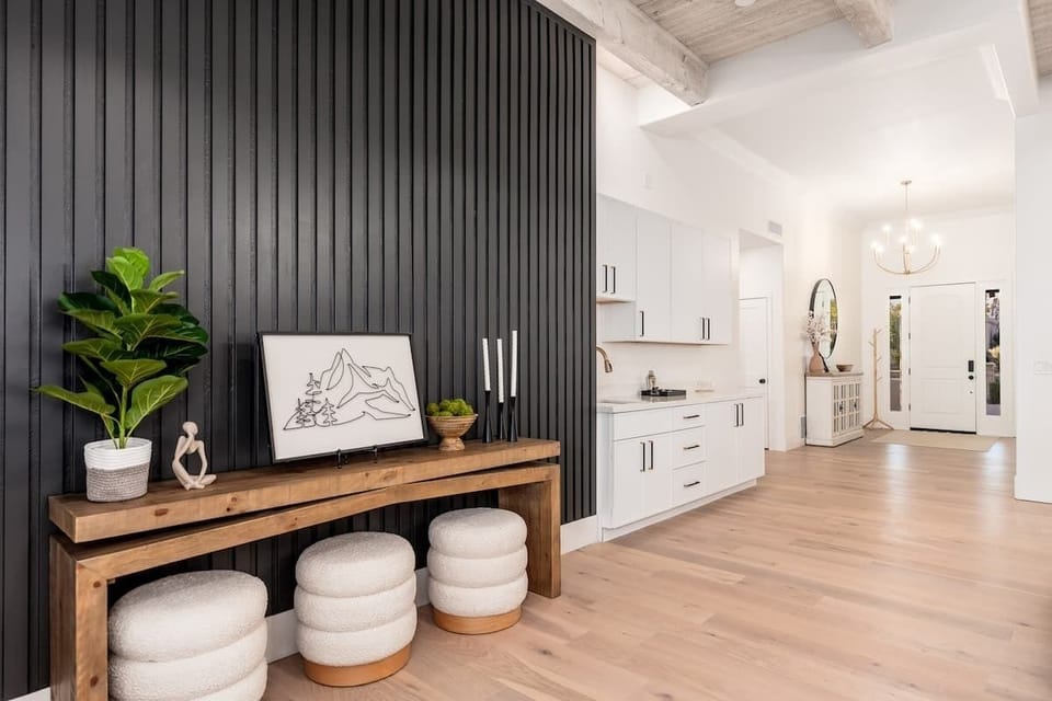 The bright, airy living space blends modern design with natural warmth. Exposed wood beams, sleek white cabinetry, and a striking charcoal accent wall create a welcoming retreat for your stay.