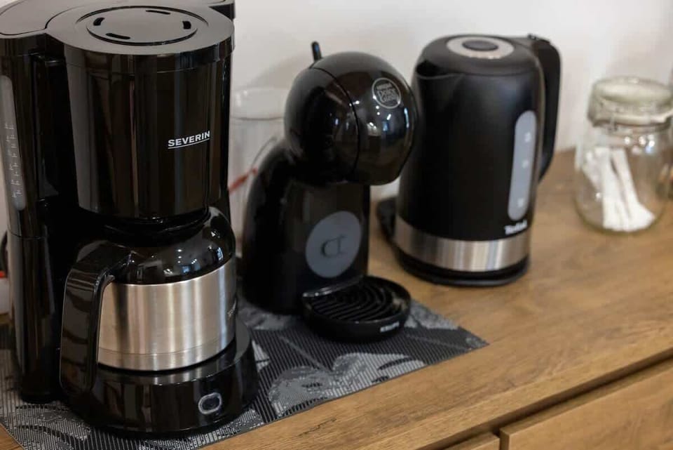 A close-up shot of kitchen appliances on a wooden counter, including a coffee maker, kettle, and other small appliances, showing the apartment is well-equipped.
