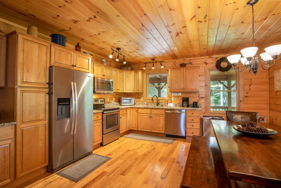 Open kitchen with stainless appliances, granite countertops and long, bench-style dining table