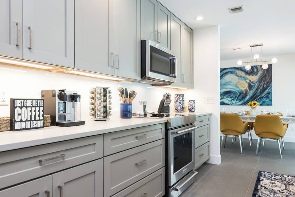 Modern kitchen with stainless steel appliances and a coffee station next to a bright dining area.