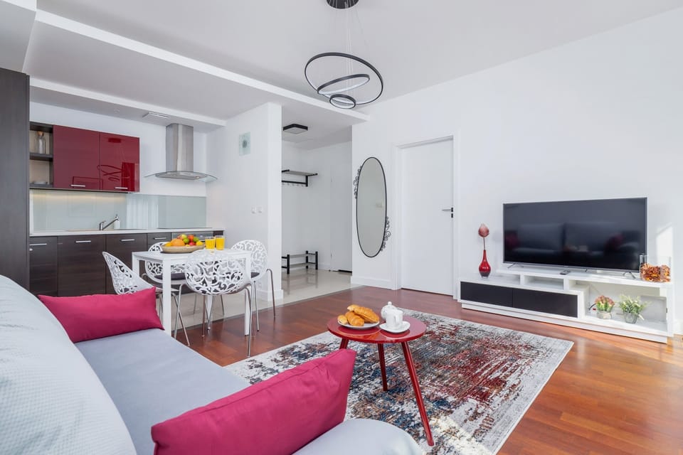Another view of the living room, showcasing the dining area with chairs and a table. The bright space is complemented by vibrant wall art and a large window.
