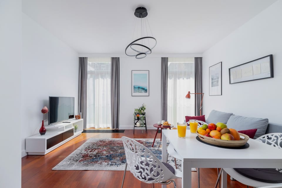 The dining and living space combined, highlighting the dining table with a fruit bowl centerpiece, large windows, and wooden flooring.