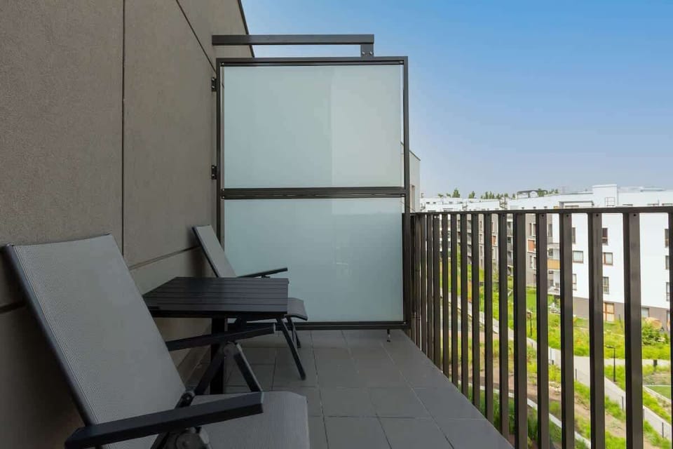 A balcony with modern outdoor seating, offering a peaceful place to relax, with a view of the surrounding area and greenery in the distance.