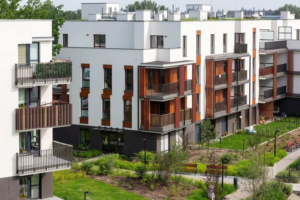 A view of a contemporary apartment building with a modern architectural style, featuring balconies and surrounded by green landscaping in an urban environment.