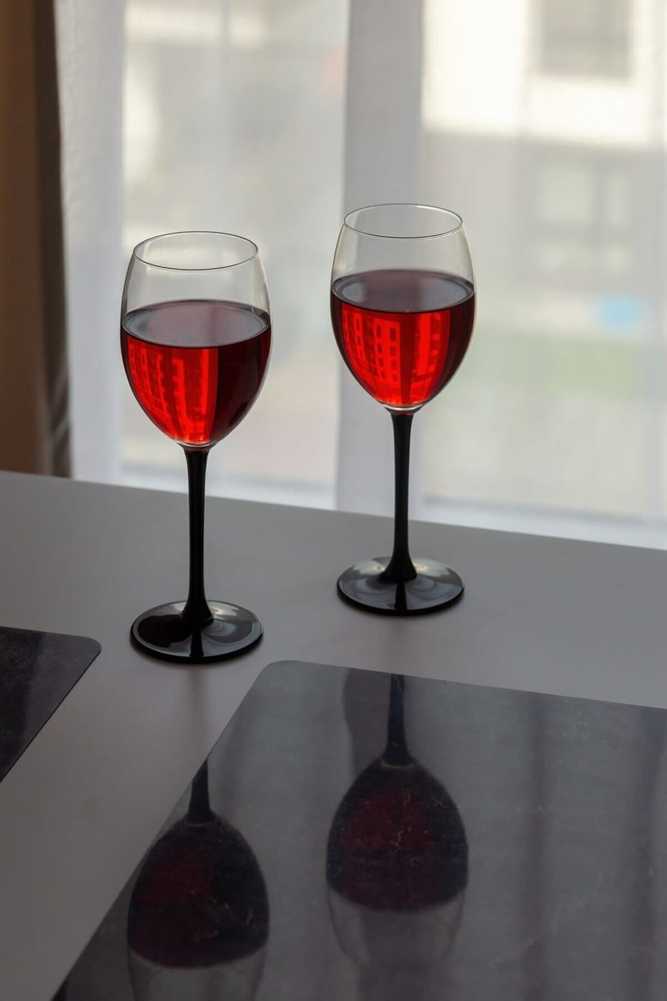 Two elegant wine glasses filled with red wine, resting on a dark table, creating a romantic or celebratory ambiance.