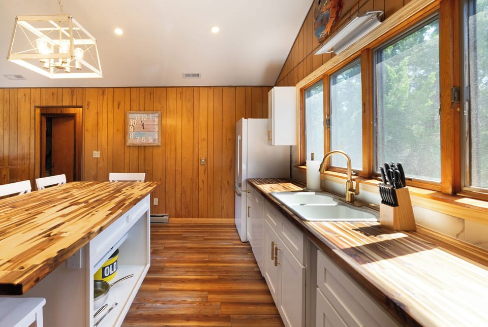 Your sunlit kitchen features warm wood counters and white cabinetry, perfect for preparing meals while enjoying nature views.