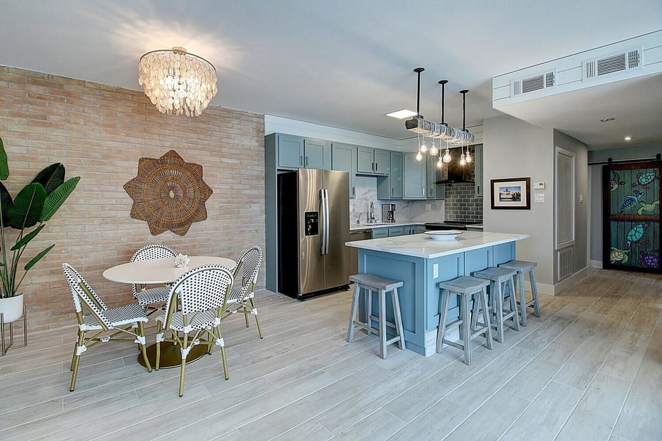 Your stylish kitchen flows seamlessly into the dining area, featuring elegant blue cabinetry, gleaming quartz countertops, and charming cafe seating.