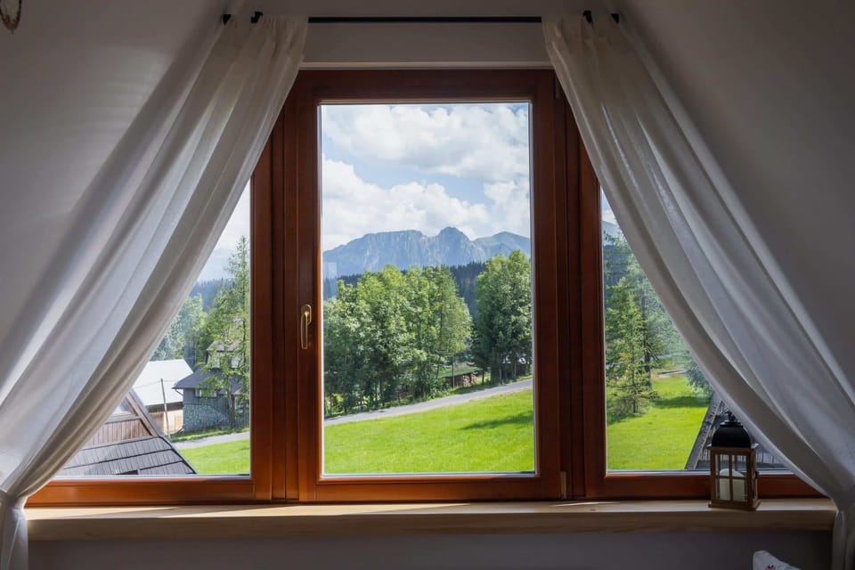  A picturesque view of rolling hills and greenery through a wide wooden-framed window.