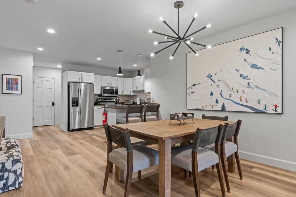 Gather around this inviting dining table where your group can share meals and stories beneath a striking modern chandelier, with a fully-equipped kitchen steps away for easy entertaining.