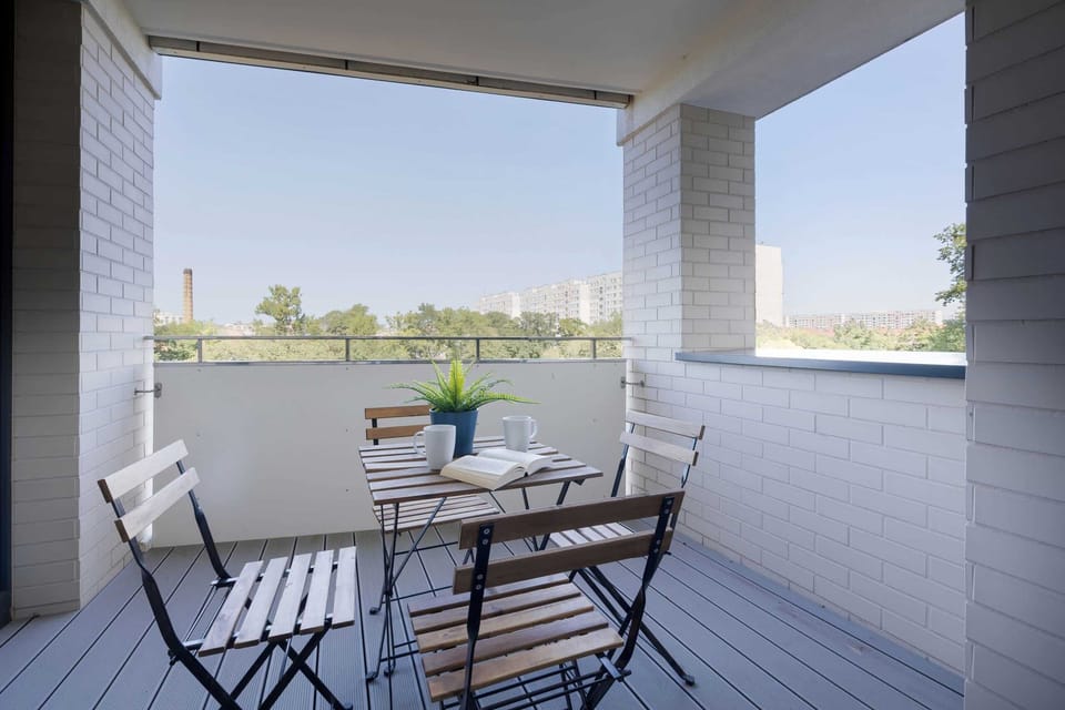  A cozy balcony setup with a table and chairs, overlooking a vibrant urban landscape.