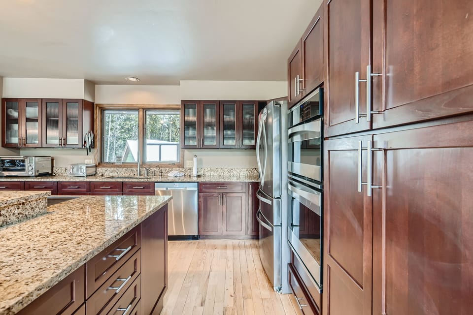 Modern kitchen with wooden cabinets, stainless steel appliances, granite countertops, and large windows.