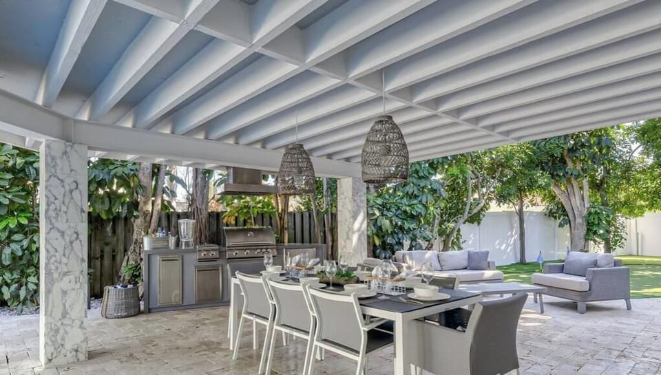 Daytime View of the Outdoor area with outdoor kitchen, dining table, lounge area, 70' outdoor TV, Putting green, Sonos, Oversized Pool & 20 Person Hot Tub/ Kiddie Pool.
