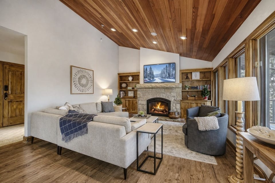 Settle into your cozy living room where the stone fireplace crackles warmly beneath wood-beamed ceilings, creating the perfect mountain retreat atmosphere.