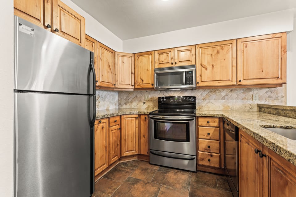 The fully equipped kitchen with wood cabinetry, granite countertops, and stainless steel appliances.