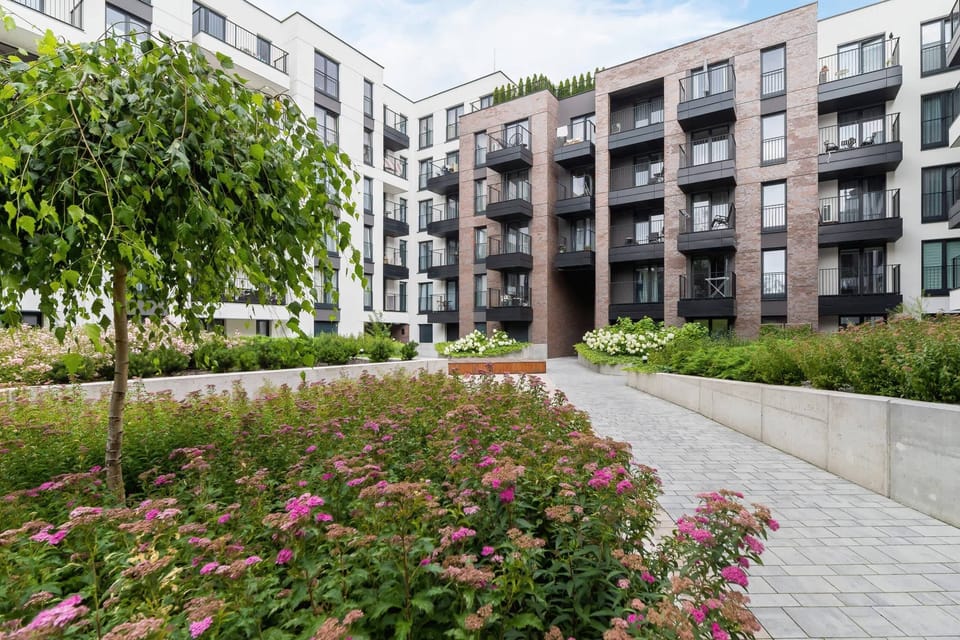 A vibrant outdoor garden surrounded by modern apartment buildings, with blooming flowers and neatly maintained greenery.