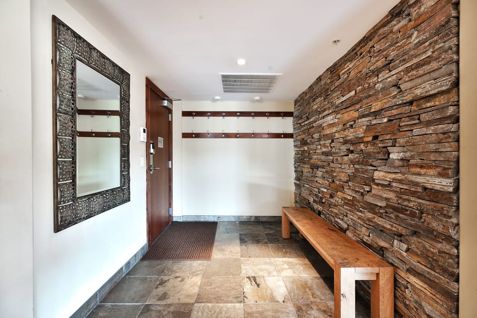 Entryway with two coat racks, wooden bench, slate stone tile floor and wall