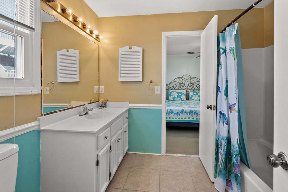 Bathroom with a yellow wall, teal wainscoting and a lit mirror at Dog Days of Summer, Cherry Grove
