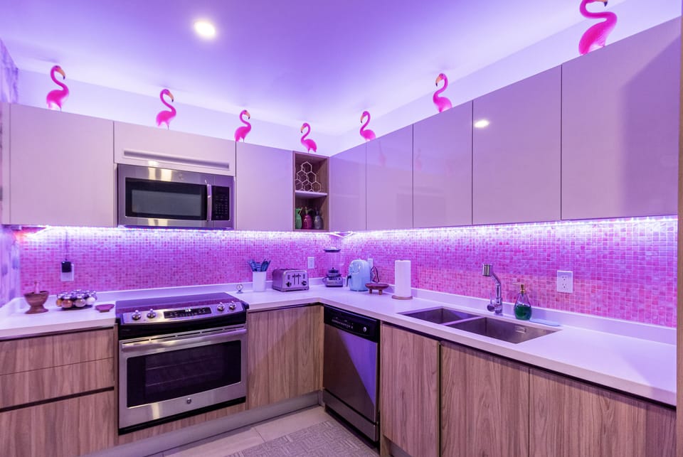 Your vibrant kitchen glows with playful pink lighting and flamingo accents, featuring modern appliances, ample counter space, and a fun, tropical vibe perfect for vacation cooking.