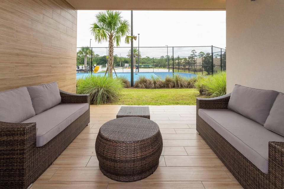 Relax on the covered patio with comfy rattan sofas and wood-look tile, overlooking palm-framed sports courts. Perfect for morning coffee or sunset chats.