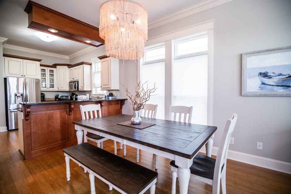 Gather around your elegant dining table beneath a stunning chandelier. The open kitchen invites cooking together while natural light creates warmth.