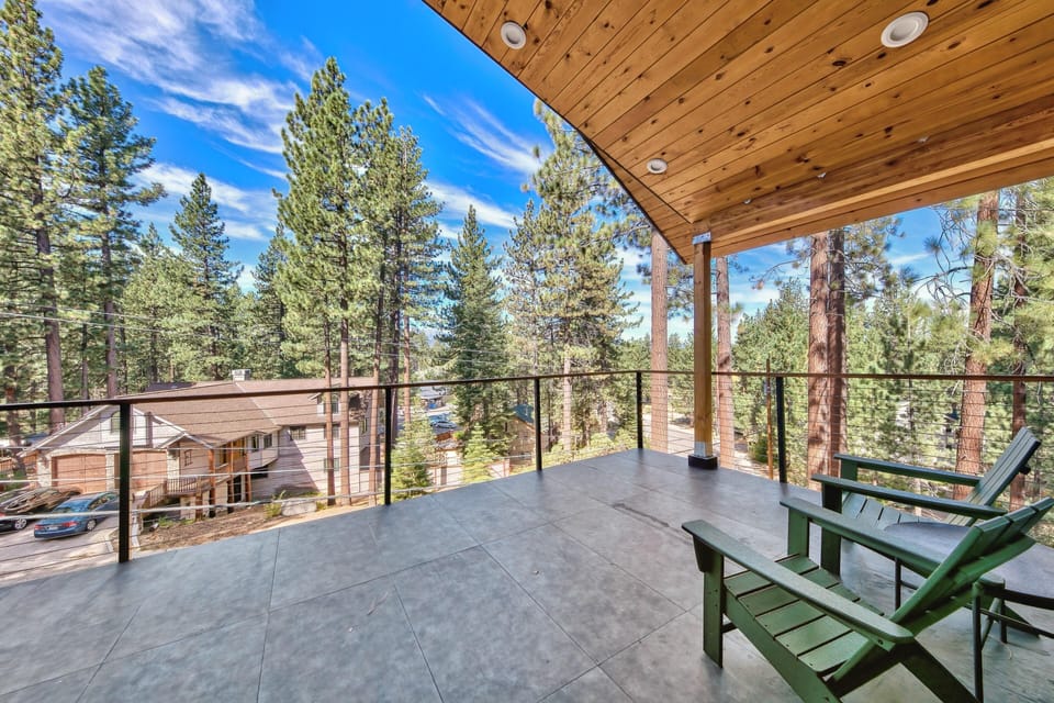 Covered balcony with large gray tile flooring, wood plank ceiling, cable railing, and two green Adirondack chairs.