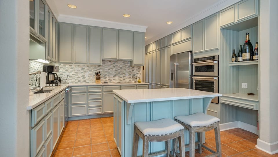 The glass-front upper cabinets offer elegant display space, while the mosaic tile backsplash adds texture and style.