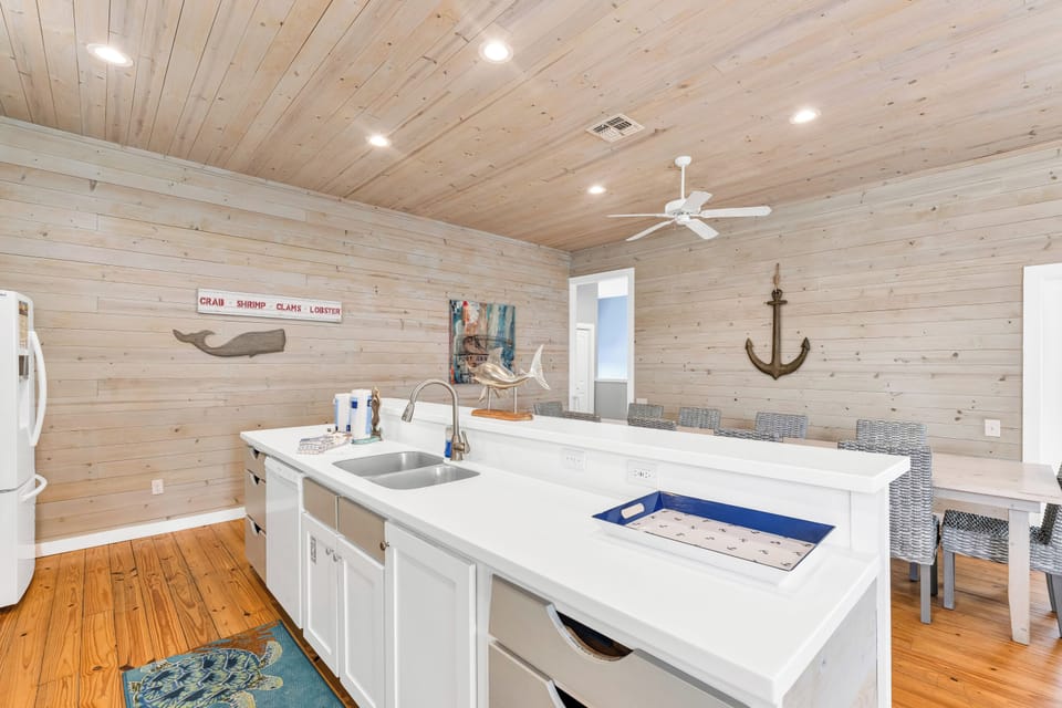 Your coastal kitchen invites you to cook with nautical charm - whitewashed wood walls, modern appliances, and dining space perfect for seafood feasts.
