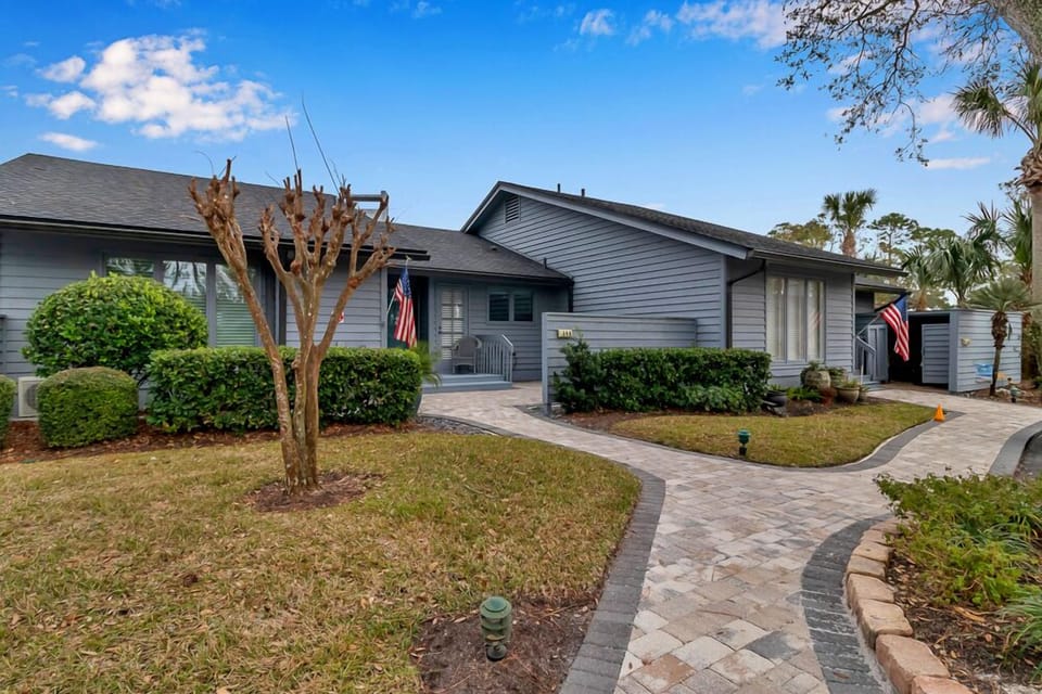 Charming entryway with curved paver path, manicured hedges, and coastal gray exterior.
