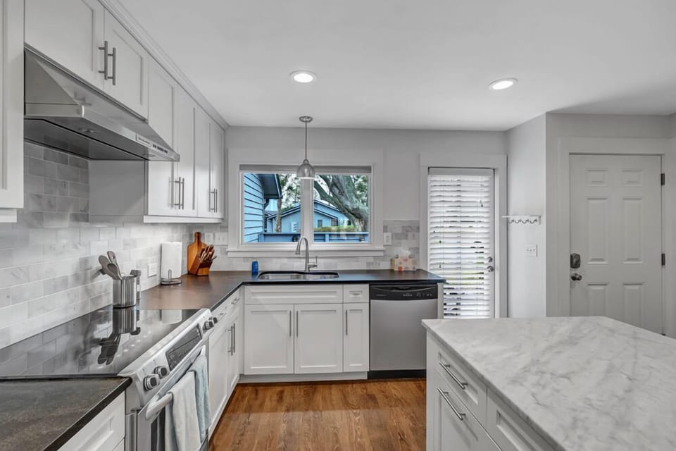 - Sleek kitchen featuring white shaker cabinets, subway tile backsplash, and stainless steel appliances
- Marble style countertops and a large window create a bright, polished atmosphere
- Convenient layout includes dishwasher and direct patio access