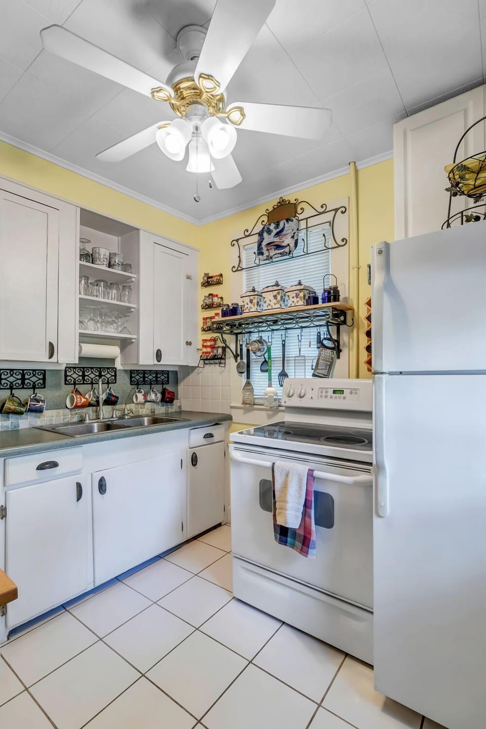- Make home cooked meals with ease in this cheerful space with stove, fridge, and open shelving
- Vibrant mugs, plates, and personal touches add warmth to every meal
- Fully stocked kitchen with plenty of character and convenience