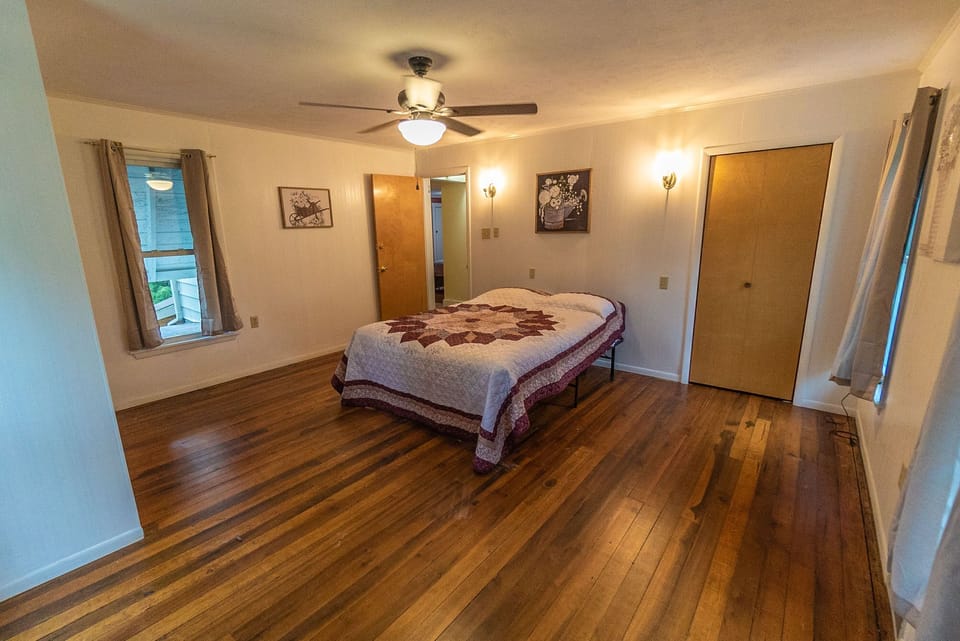 Cozy wood bedroom with a television, three windows and ceiling fan with captivating window views.