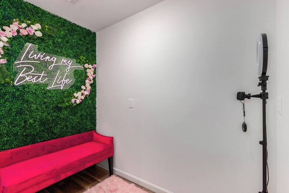 In the secret room, you'll find a bright pink neon "Living my Best Life" neon sign, set against a floral wall, which is the perfect place for a picture! Place your phone on the ring light stand, and use the Bluetooth remote to take pictures!