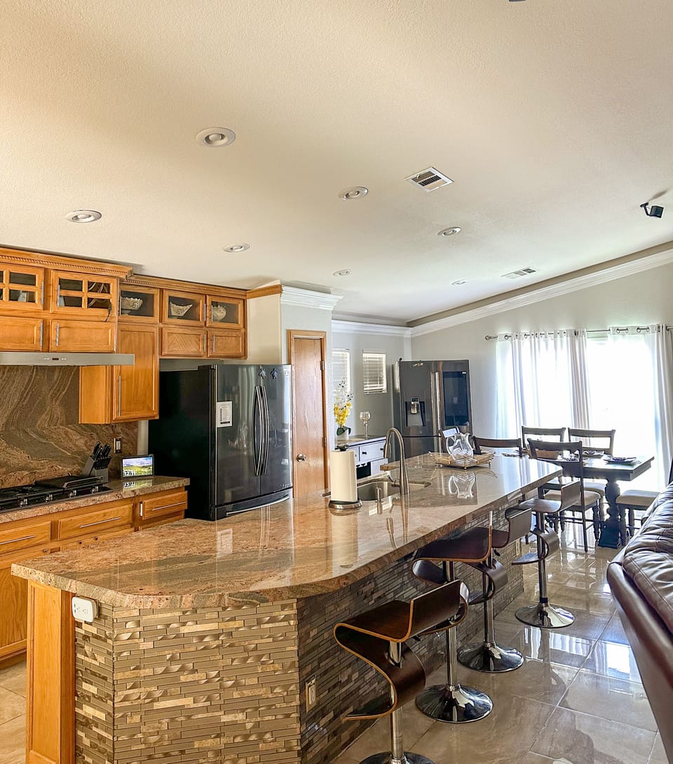 Kitchen and  countertop with 6 outlets underneath and 3 bar chairs.