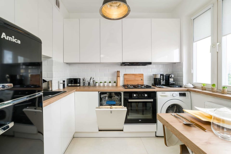A modern kitchen with white cabinets, a wooden countertop, and sleek black appliances.
