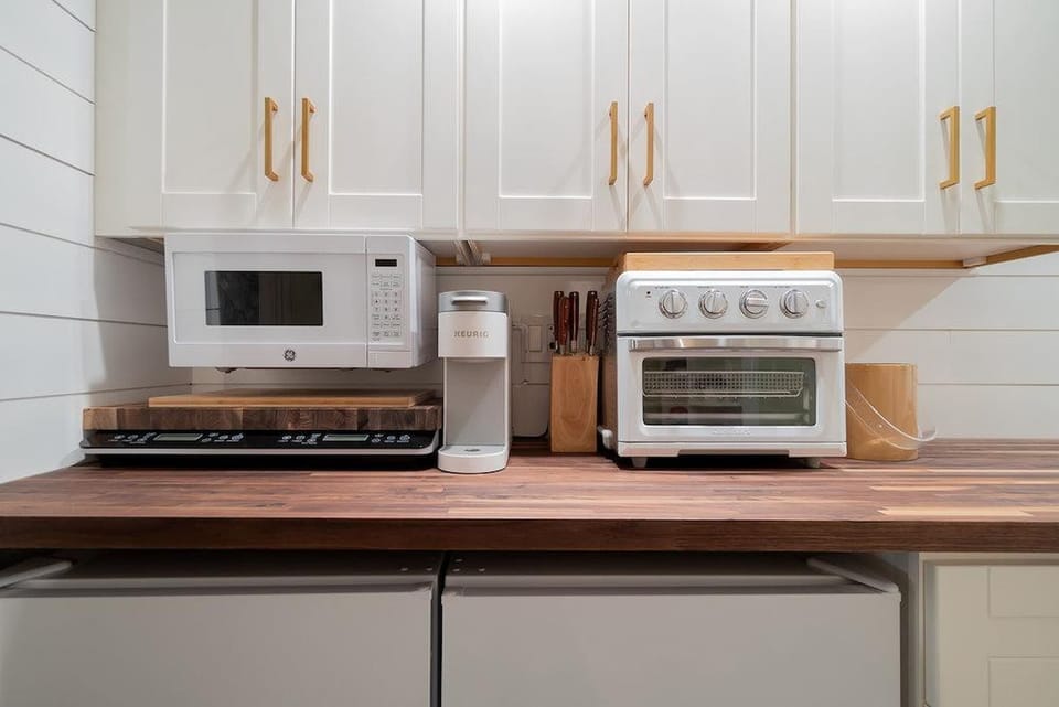 Kitchenette with a Toaster oven, microwave, mini fridge, Keurig coffee maker, glasses, plates, and cutlery. 