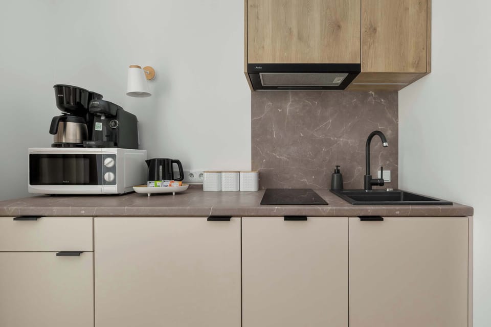 A kitchenette corner displays a coffee machine, microwave, sink, and storage cabinets. Compact appliances maximize functionality.