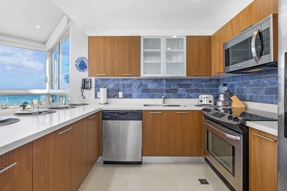 Step into your fully equipped coastal kitchen where ocean views frame every meal you'll prepare. Modern appliances and sleek finishes make cooking a pleasure while turquoise waters shimmer just beyond the window.