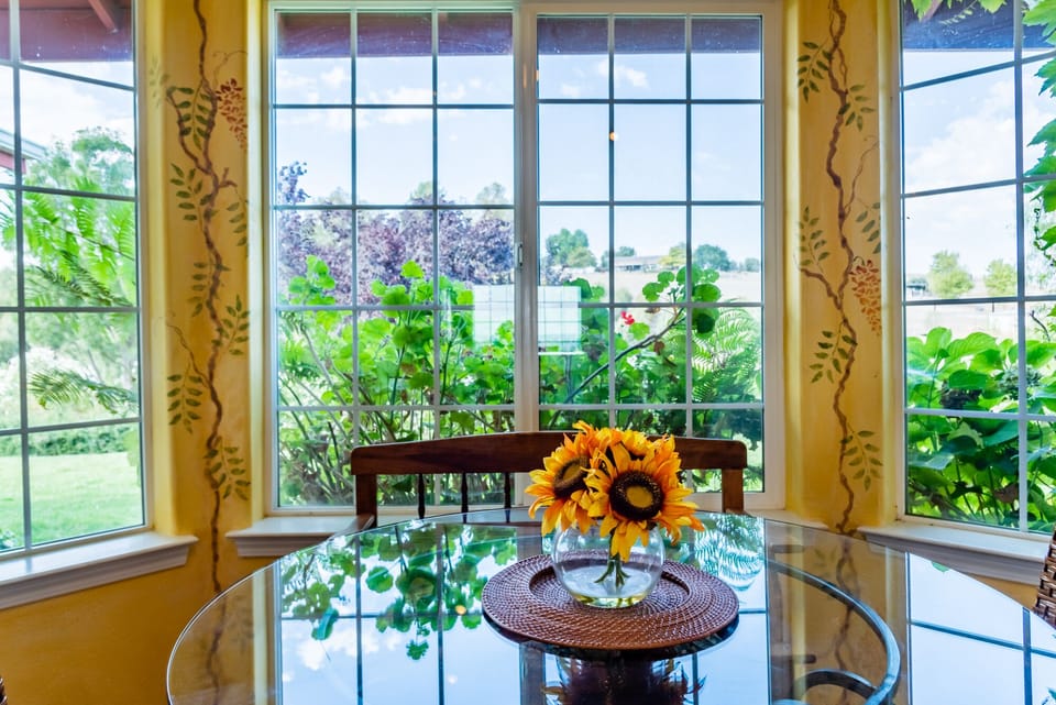 A round glass table sits in a bright nook with garden views.