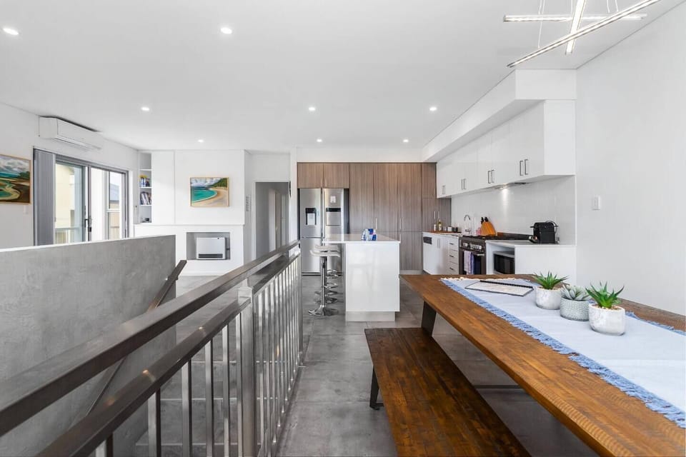Spacious contemporary kitchen with an adjoining wooden dining table near the staircase—ideal for gathering, cooking, and enjoying meals in a stylish and functional setting.