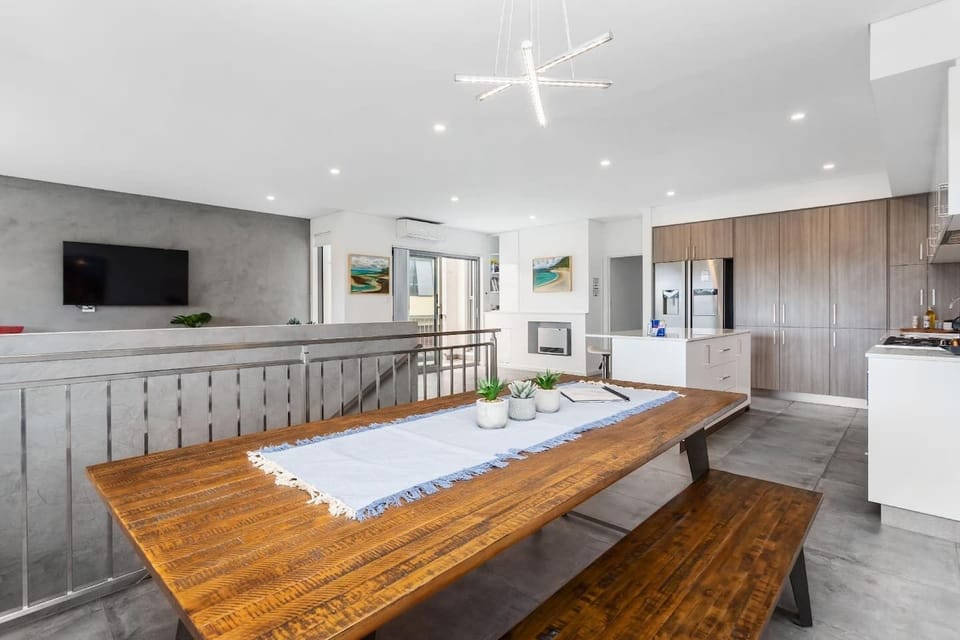 Bright open-plan kitchen and dining area featuring a large rustic wooden table, modern cabinetry, and sleek finishes—perfect for family meals or entertaining, all just steps from the staircase for easy flow throughout the home.