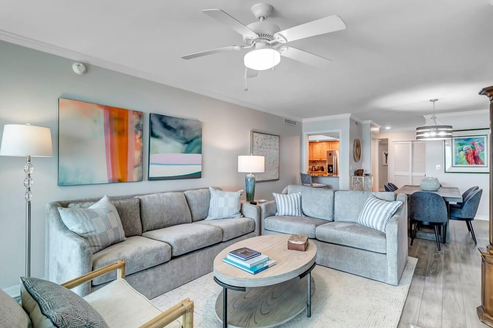 - Open concept living room with plush sofas, modern art, and a neutral beach palette
- Ceiling fan and natural light keep the space breezy and comfortable
- Flows effortlessly into the dining area and kitchen for easy entertaining