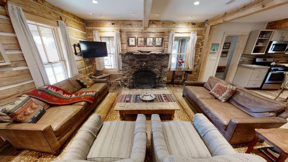 Gather around the rustic stone fireplace in this inviting living room, where warm wood beams and plush seating create your perfect mountain retreat for cozy evenings together.