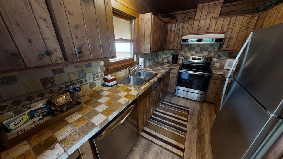 Cook your favorite meals in this charming rustic kitchen with modern appliances, including a stainless steel stove and fridge, stone countertops, and cozy cabin-style wood paneling throughout.