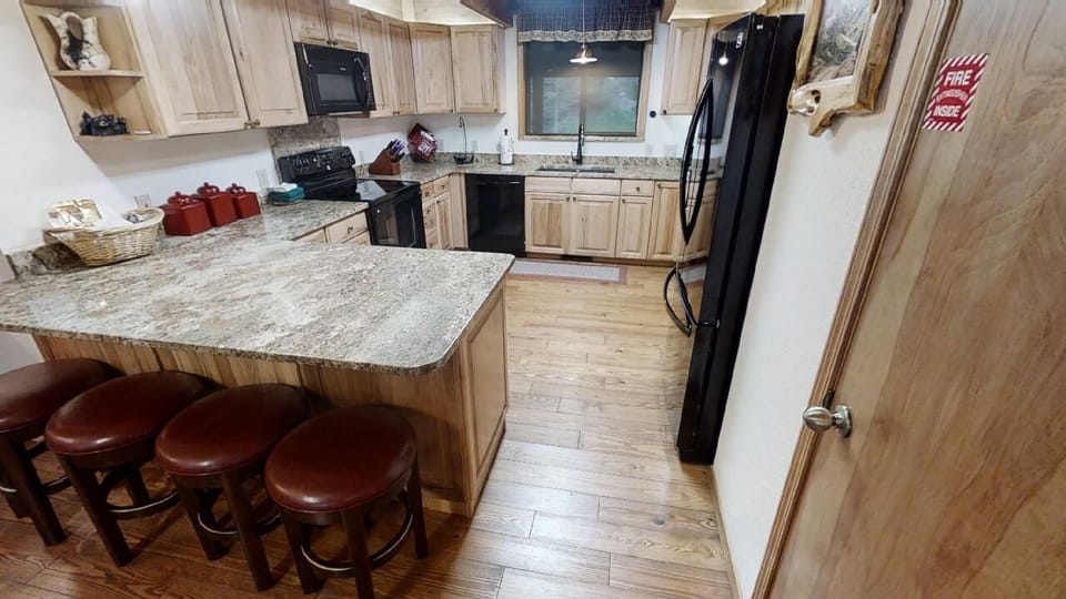 Your fully equipped kitchen features granite counters, a breakfast bar with seating, modern black appliances, and warm wood cabinetry—perfect for preparing meals together or sipping morning coffee before your mountain adventures.