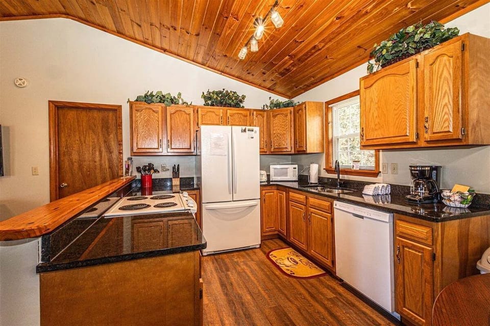 Full kitchen featuring natural wood cabinets, white appliances, dark countertops, and wood ceilings. Conveniently located near Bryson City and popular Smoky Mountain destinations.