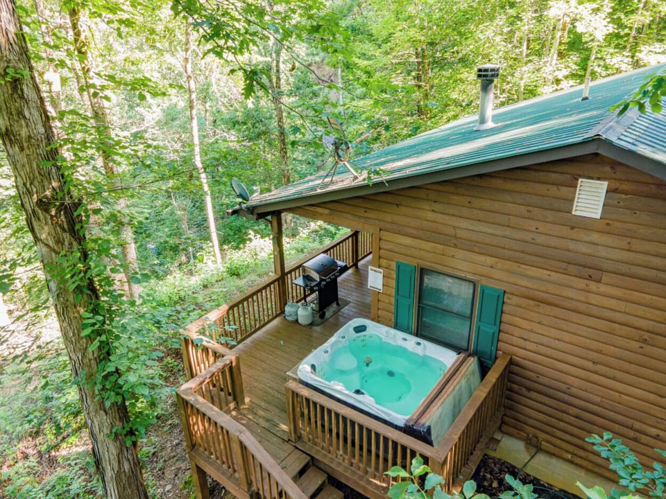 The elevated deck features a private hot tub beside the cabin with wooded surroundings. Guests can unwind in a peaceful Smoky Mountain setting near Bryson City.