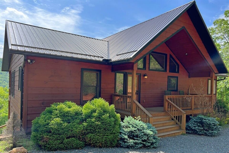 The front porch entry of Smoky Mountain High welcomes guests with a classic log cabin design and landscaped greenery set against the Smoky Mountains.