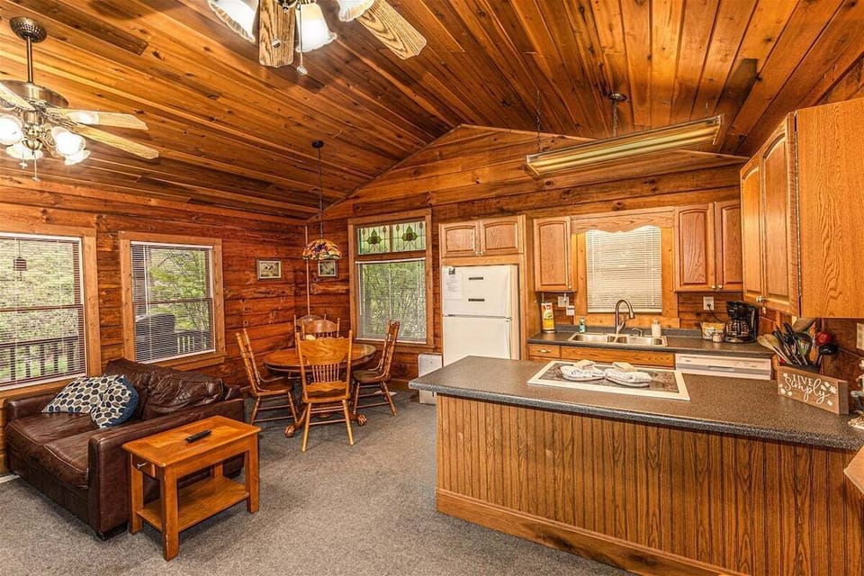 Open-concept living area with a kitchen island, dining space, and wood-paneled interior at this Bryson City cabin retreat. Comfortable seating and large windows bring natural light into the main gathering space.