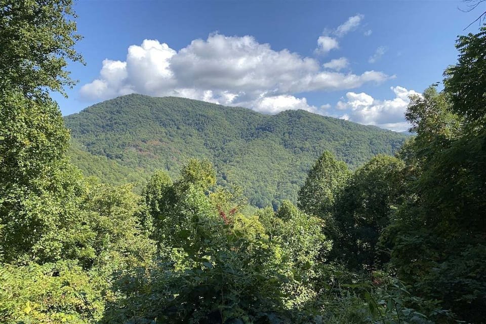 Expansive view of green mountain ridges beneath a blue sky with scattered clouds. The property offers sweeping Smoky Mountain vistas.